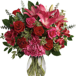 Bouquet of pink lilies, red roses, and pink hydrangeas in a glass vase