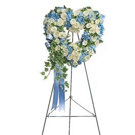Heart-shaped floral wreath on a black stand with blue ribbon