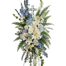 Standing floral spray with white lilies, cream roses, and blue flowers around a cross