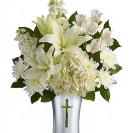 White lilies and daisies arranged in a clear vase with a cross emblem