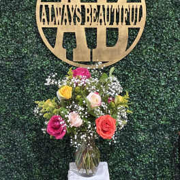 Mixed rose bouquet in a glass vase beneath a gold monogram sign