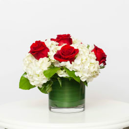 Red roses and white hydrangeas in a green glass vase