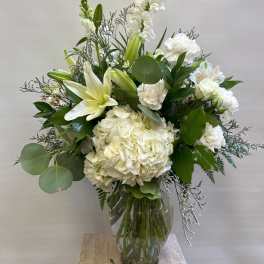 White floral arrangement in a clear glass vase with lilies and hydrangea