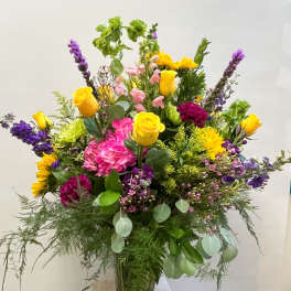 Mixed bouquet of yellow roses, pink hydrangea, and purple flowers in a glass vase