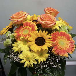 Bouquet of orange roses and yellow gerbera daisies in a glass vase