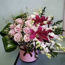Pink roses and magenta lilies arranged in a pink hatbox