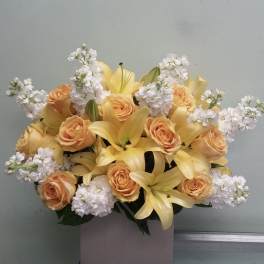 Bouquet of yellow lilies, peach roses, and white blossoms in a box