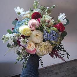 Handheld bouquet of mixed roses, hydrangeas, and white daisies