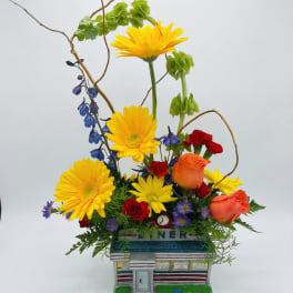 Colorful flower arrangement in a diner-shaped container with a blue toy car