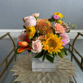 Mixed bouquet with sunflowers, roses, and carnations in a square vase