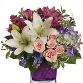 Bouquet of white lilies, pink roses, and purple flowers in a purple vase
