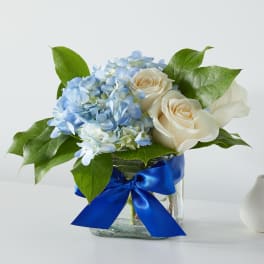 Blue hydrangea and cream roses in a glass vase with a blue ribbon