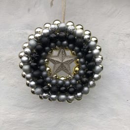 A circular ornament wreath with black, silver, and gold baubles and a star center