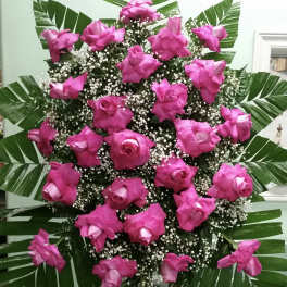 Tall standing spray of pink roses with baby's breath and palm leaves