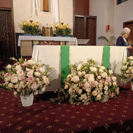 Three white floral arrangements with pale pink roses at an altar