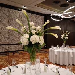 Tall white floral centerpiece in a clear glass vase on a banquet table