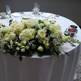 White floral centerpiece on a round table with glassware and place settings