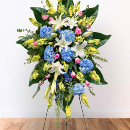 Standing floral spray with blue hydrangeas, white lilies, and yellow snapdragons