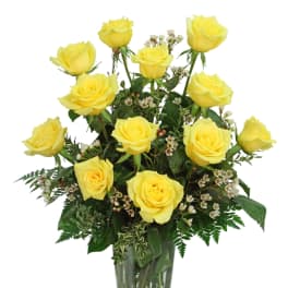 Yellow roses arranged in a clear glass vase with greenery