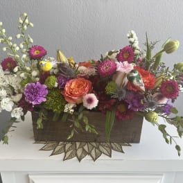 Mixed floral arrangement in a wooden box with pink, orange, white, and purple blooms