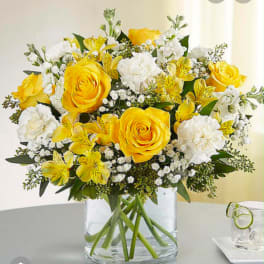Yellow roses and white flowers in a clear glass vase
