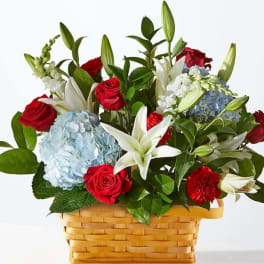 Basket arrangement of red roses, white lilies, and blue hydrangeas