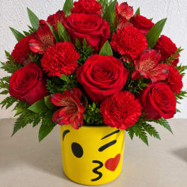 Red roses and carnations in a yellow emoji mug vase