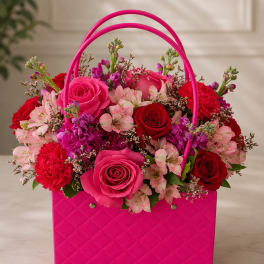 Pink handbag-style box filled with roses, carnations, and alstroemeria
