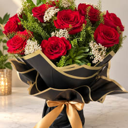 Bouquet of red roses wrapped in black paper with a gold ribbon