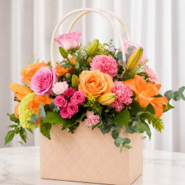 Colorful flower arrangement in a quilted peach basket with arched handles