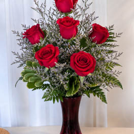 Red roses arranged in a tall vase with greenery