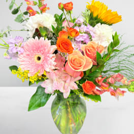 Mixed bouquet of pink, orange, yellow, and white flowers in a glass vase