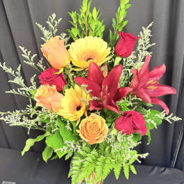 Mixed bouquet of roses, gerbera daisies, and lilies in a glass vase