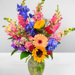 Colorful mixed bouquet in a clear glass vase with sunflowers and gerbera daisies