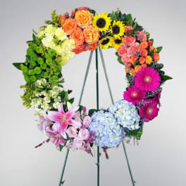 Large multicolored floral wreath on a stand with roses, lilies, sunflowers, gerbera daisies, and hydrangeas.