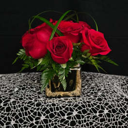 Red roses arranged in a gold square vase with green foliage