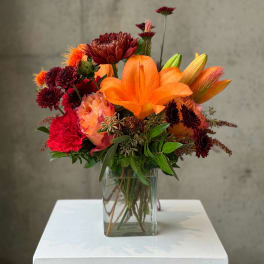 Orange lilies and mixed red flowers in a clear glass vase