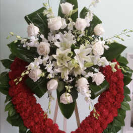 Heart-shaped floral wreath with white roses and lilies on a stand