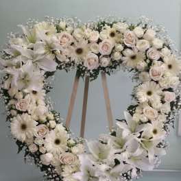 Heart-shaped floral wreath with white lilies, roses, and daisies on an easel