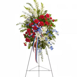 Standing floral spray with red carnations, white lilies, and blue accents on an easel
