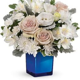 White and blush flower arrangement in a blue glass vase