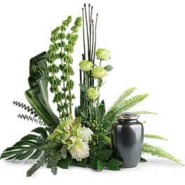 Green floral arrangement with orchids and a dark urn vase