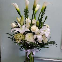 White calla lilies and roses arranged in a glass vase with a lavender ribbon
