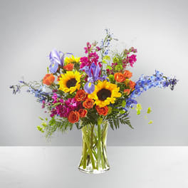 Colorful bouquet with sunflowers, roses, irises, and blue flowers in a clear vase