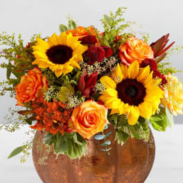Orange roses and sunflowers arranged in a copper pumpkin vase