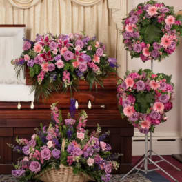 Funeral casket surrounded by purple and pink floral sprays and wreaths