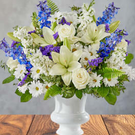 White lilies, roses, daisies, and blue flowers in a white vase