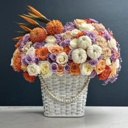 Basket arrangement of roses, dahlias, and small pumpkins