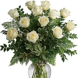 White roses arranged in a clear glass vase with dense greenery