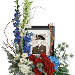 Floral tribute with red and white roses around a framed military portrait